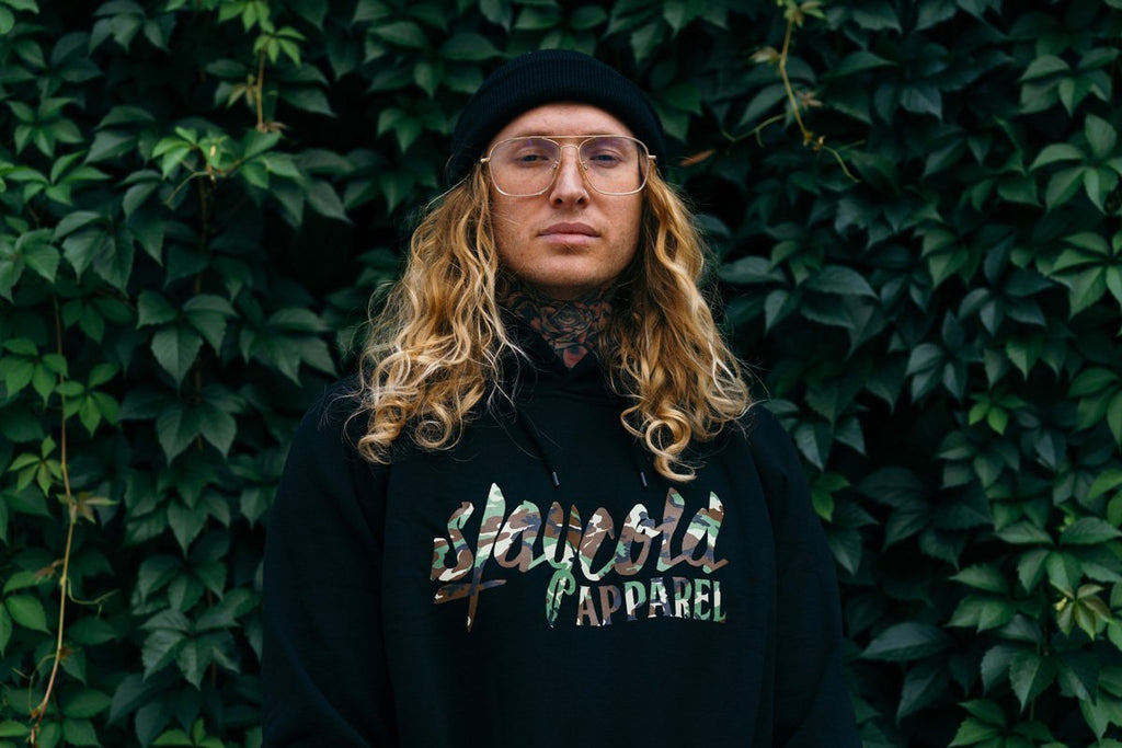 Male tattooed Model wearing the new Stay Cold Apparel Variation of the Essential Logo Hoodie in Camouflage Woodland