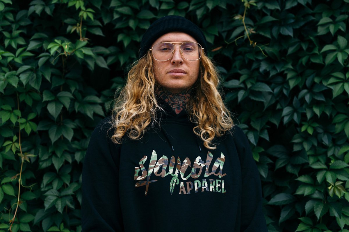 Male tattooed Model wearing the new Stay Cold Apparel Variation of the Essential Logo Hoodie in Camouflage Woodland