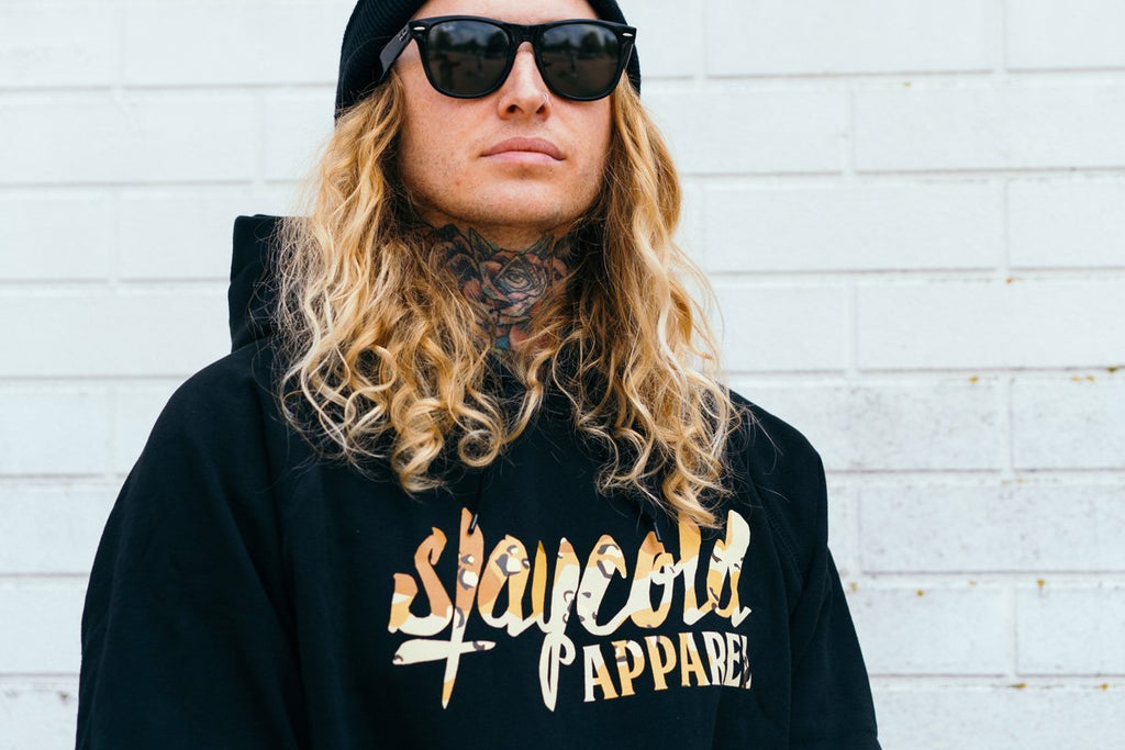Male tattooed Model in sunglasses wearing the new Stay Cold Apparel Variation of the Essential Logo Hoodie in Camouflage Desert Storm