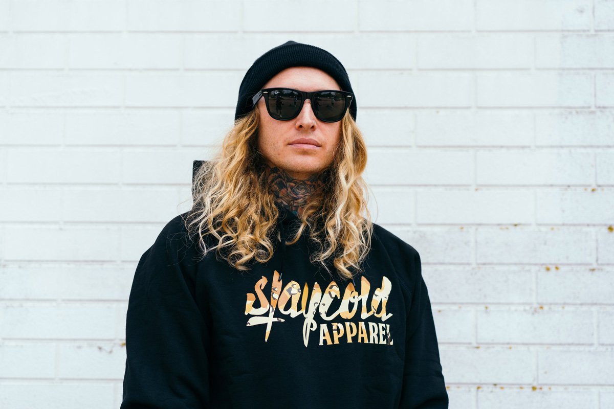 Male tattooed Model in sunglasses wearing the new Stay Cold Apparel Variation of the Essential Logo Hoodie in Camouflage Desert Storm